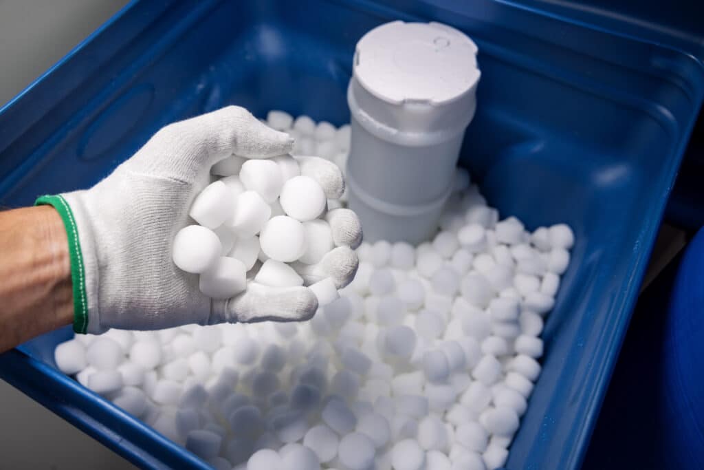 Gloved hand holds salt tablets above an opened water softener filled with salt
